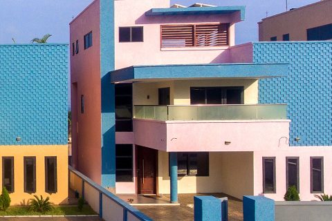 Front of an apartment building in pink with a glass balcony